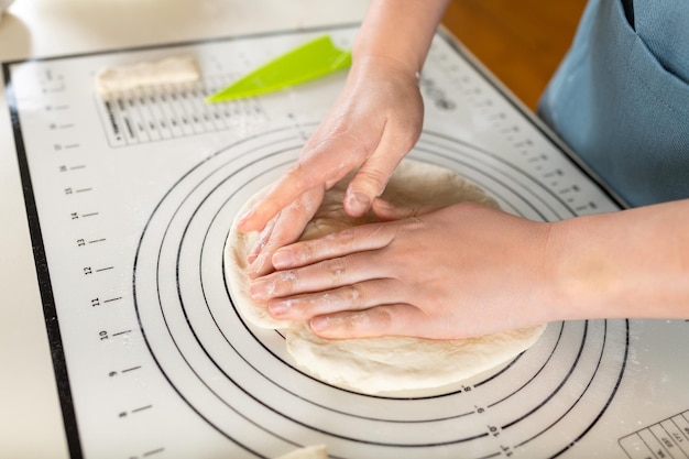 Closeup on female hands crumpling fresh kneaded dough on a kitchen baking mat