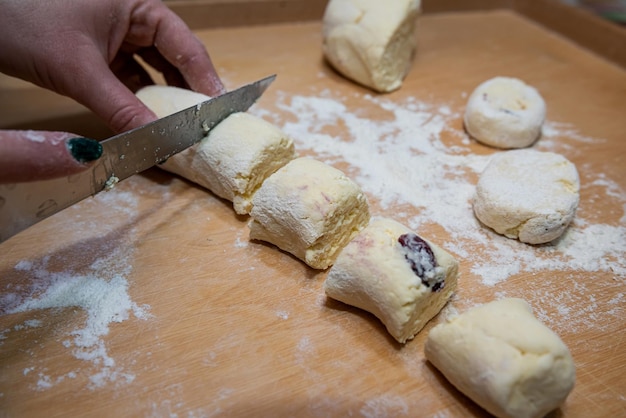 Closeup of female hands in flour with a knife cut dough sausage in small pieces