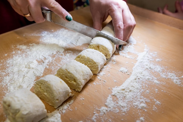 Closeup of female hands in flour with a knife cut dough sausage in small pieces