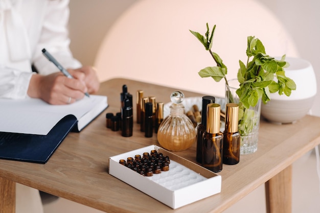 Closeup of female hands holding a bottle of essential oil and writing an entry in a notebook aromath