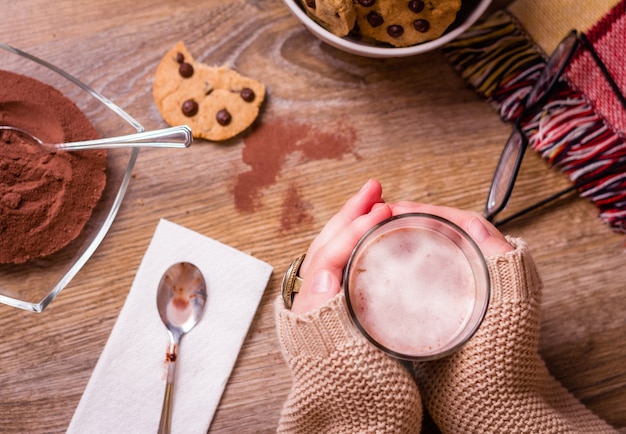 Closeup of female hands holding hot drink glass over a table with chocolate chip cookies on stars bowl