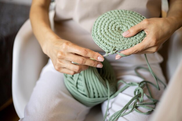 Photo closeup female hands knitting interior decor basket use green ribbon yarn and crochet needle creative woman arms enjoying needlecraft hobby or art work making comfortable cotton sewing accessories