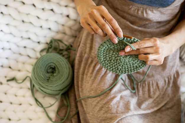 Photo closeup female hands knitting interior decor basket use green ribbon yarn and crochet needle