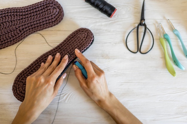 Closeup female hands knitting wool slippers sewing connecting sole and yarn use threads needle