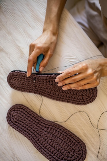 Closeup female hands knitting wool slippers sewing connecting sole and yarn use threads needle