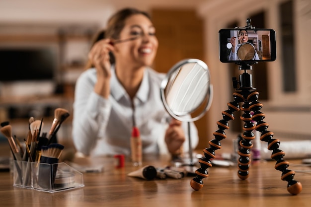 Closeup of female influencer using mascara while vlogging about makeup at home