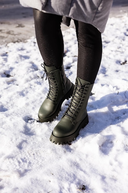 Closeup of female legs in green boots standing in the snow Women's leather winter shoes