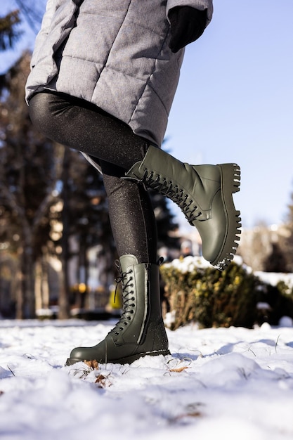 Closeup of female legs in green boots standing in the snow Women's leather winter shoes