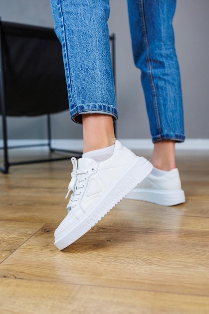 Closeup of female legs in jeans and casual white sneakers Women's comfortable casual shoes White leather women's sneakers