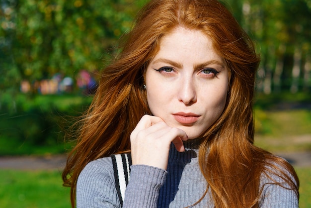 Closeup female portrait of a red-haired Caucasian woman with makeup, with green eyes looking at the front on a natural wall on a sunny day