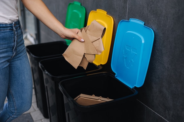 Closeup of female throwing piece of cardboard in recycling bin different colour of recycling bins