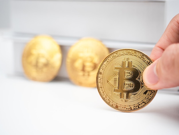 Closeup finger holding gold bitcoin on table with book background