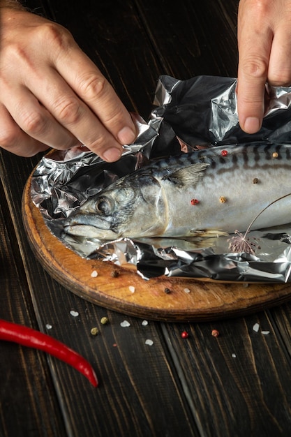 Closeup fish chef hands preparing mackerel in kitchen Wrapping fish in foil before baking in oven