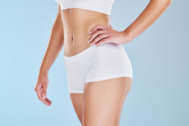 Closeup of fit woman showing her stomach and body in underwear or sportswear isolated against blue studio background with copyspace Toned sporty model standing alone Slim physique and flat tummy