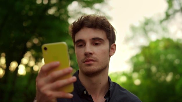 Closeup focused man using smartphone outdoors at sunset Portrait of serious man reading message online on mobile phone during walk in park Handsome male person having walk with cellphone on road