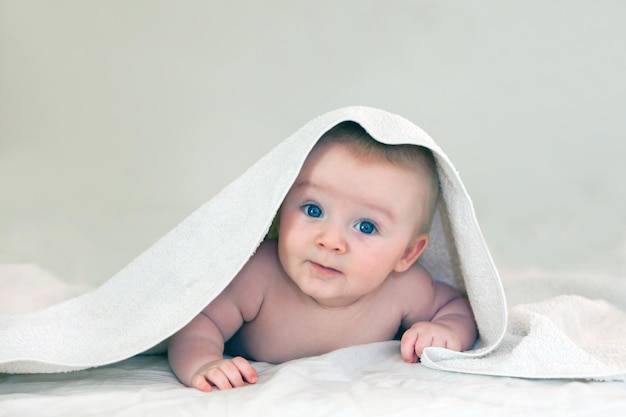 Closeup of four month old baby boy with bright blue eyes white towel on kid head