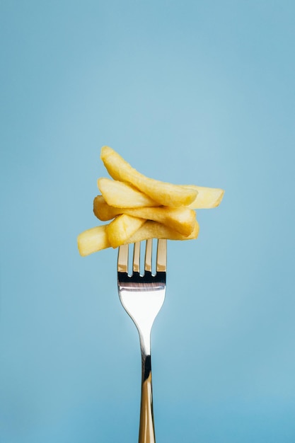 Closeup of french fries chopped on a fork on a blue background