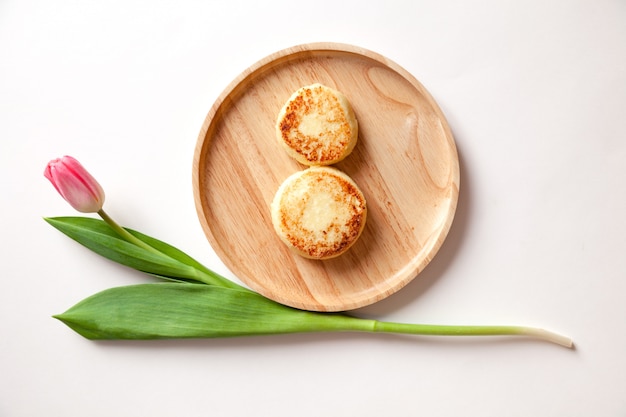 Closeup fresh flower pink tulip on wooden round plate, two golden fried cheesecakes.