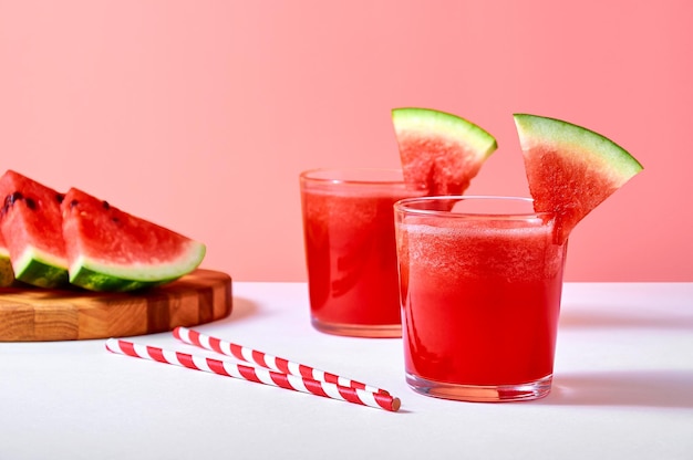 Closeup fresh watermelon juice or smoothie in glasses with watermelon pieces on pink background