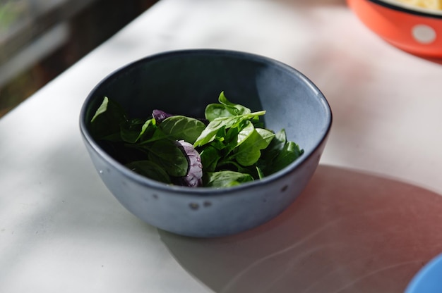 Closeup of freshly picked basil leaves fragrant culinary herbs in a navy blue ceramic bowl on white table background