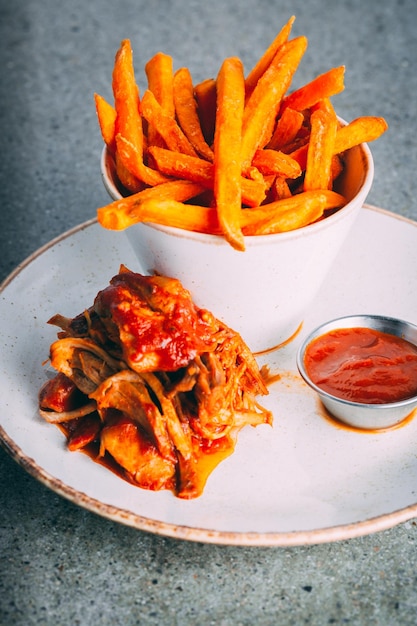 Closeup of fried potato and vegetables served with a red sauce on a white plate