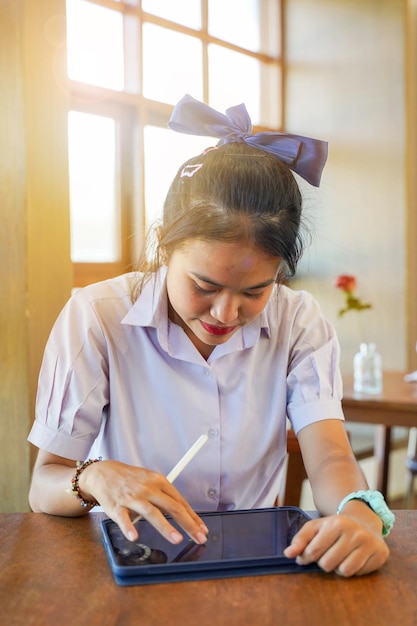 Closeup front view of Thai girl student using and study on tablet at school with sun flare