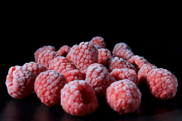 Closeup frozen raspberries on black plate and black background