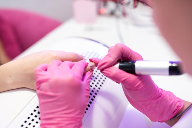 Closeup of a girl doing a manicure in a beauty salon Nail care Manicurist in pink gloves removes gel polish from nails with a fresco Hardware manicure revealed Cosmetic procedure