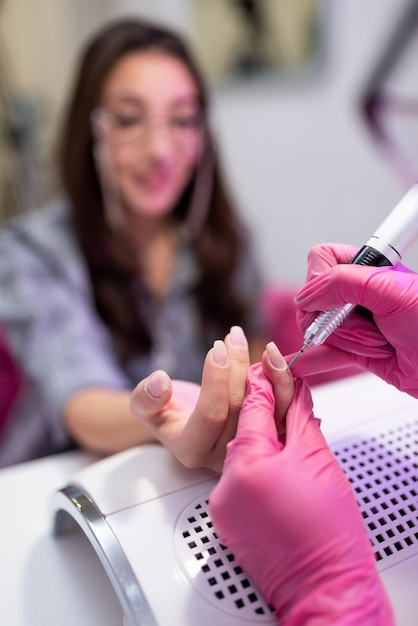 Closeup of a girl doing a manicure in a beauty salon Nail care Manicurist in pink gloves removes gel polish from nails with a fresco Hardware manicure revealed Cosmetic procedure