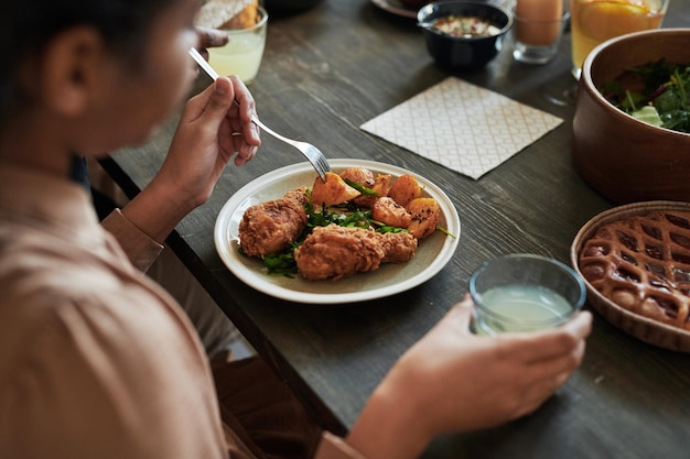 Closeup of girl sitting at table and eating chicken with potatoes during dinner