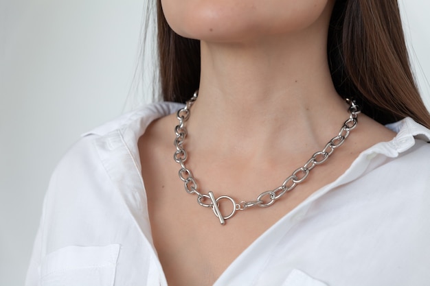 Closeup gold chain on model brunette with long hair, metal necklace, white shirt neckline