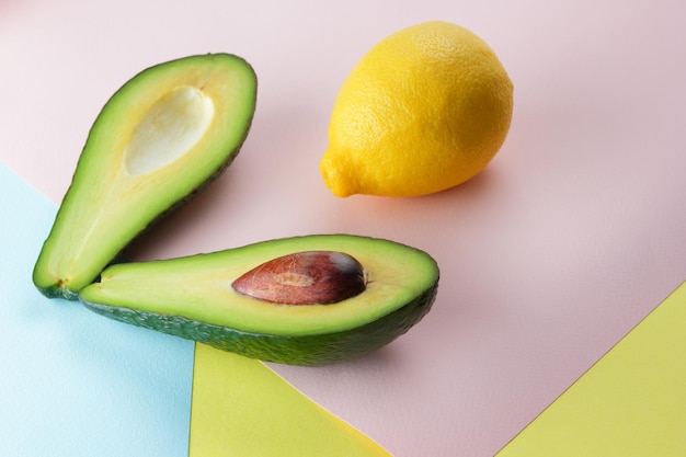 Closeup green healthy fruit with lemon on a colorful background Two halves of a ripe avocado with seed with a whole yellow lemon