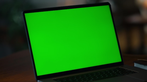 Closeup green screen computer on wooden table indoors Laptop computer with mockup display on working desk inside Laptop with chroma key screen on workplace Digital technology concept