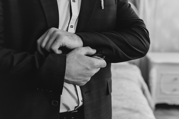 Closeup of a groom in maroon suit correcting a sleeve