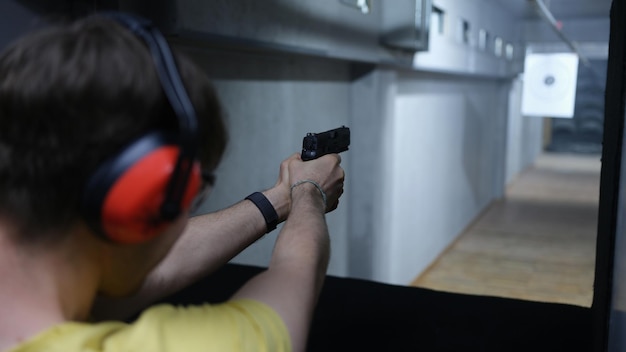 Closeup of guy in tactical headphones aiming pistol at target in shooting range shooting