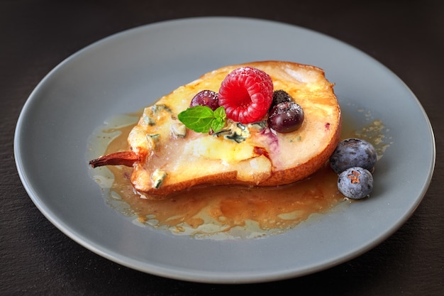 Closeup on half baked pear with blue cheese and berries on dark