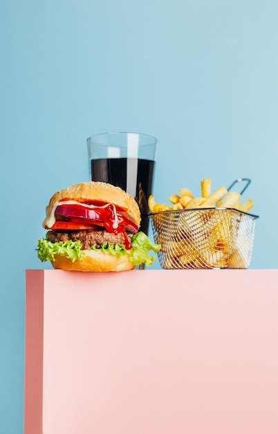 Closeup on a hamburger and french fries and soda on a pink cube on a blue background with free space for text