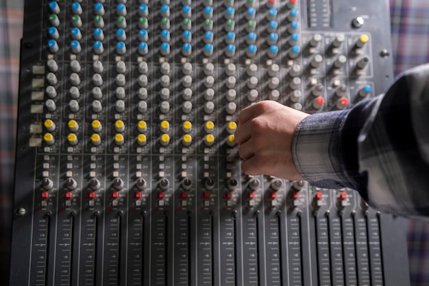 Photo closeup of a hand adjusting the controls on a music mixer console in a studio