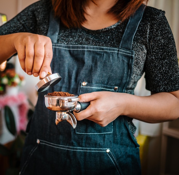 Closeup of hand barista or coffee maker holding filter and coffee tamper making an espresso coffee