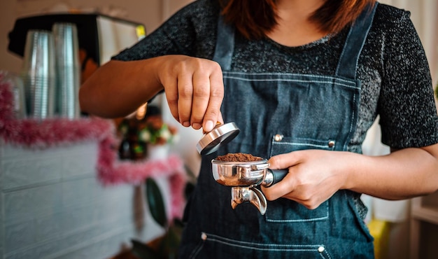 Closeup of hand barista or coffee maker holding portafilter and coffee tamper making an espresso