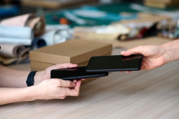 Closeup of hand of buyer holding smartphone over that of shop assistant