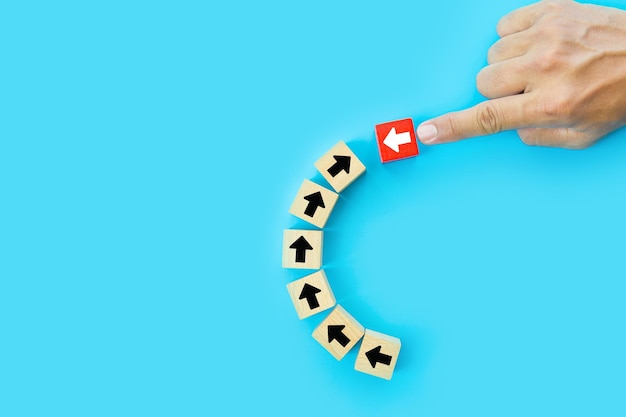 Closeup hand choose cube wooden toy block stacked with arrow icon pointing to opposite directions for way of business change leader planning company and transform concept