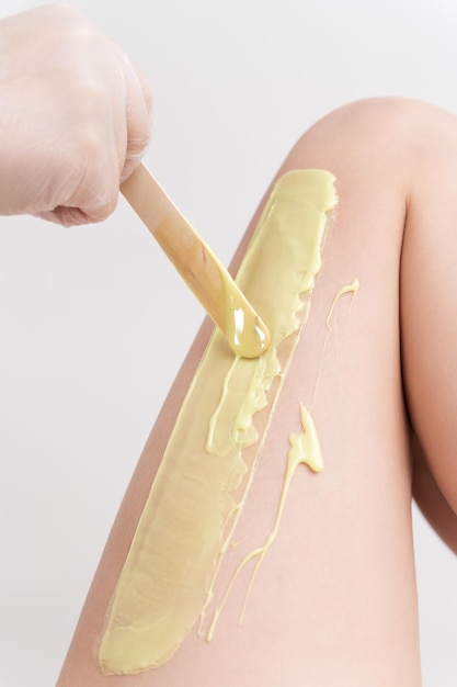 Closeup hand in glove applying hot wax on woman leg using spatula Professional depilation procedure