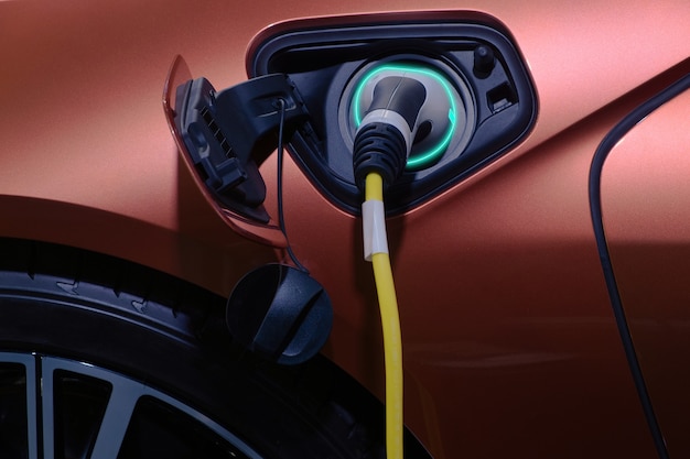 Closeup hand grip plug connected with socket charge on brown electric car for rechargeable battery