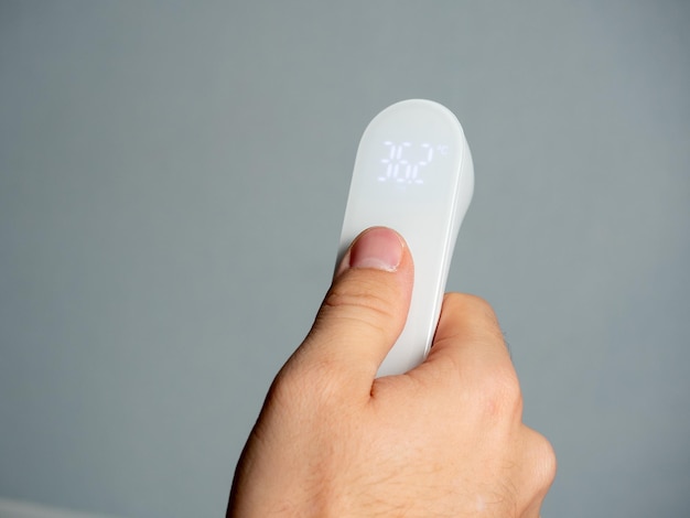 Closeup of a hand holding an electronic remote thermometer isolated on a gray background The concept of medicine diagnosis of the disease