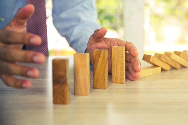 Closeup hand prevent wooden block not falling domino concepts of financial risk management and strategic planning and business challenge plan