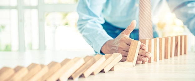 Closeup hand prevent wooden block not falling domino concepts of financial risk management and strategic planning and business challenge plan