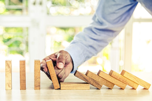 Closeup hand prevent wooden block not falling domino concepts of financial risk management and strategic planning and business challenge plan