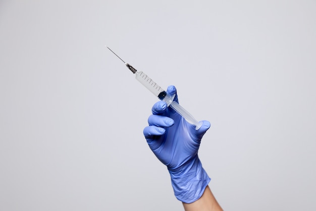 Closeup hand in rubber latex medicine purple glove holding transparent syringe with a sharp needle