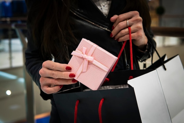 Closeup of the hand of a young caucasian woman with her fingernails painted red holding a black shopping bag of gifts. Buying gifts for the new year and Christmas at the Mall.